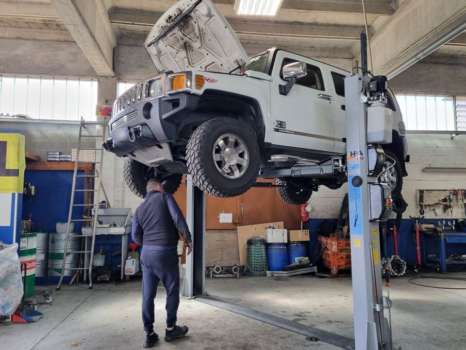 Fuoristrada bianco sul ponte sollevatore e meccanico al lavoro in officina